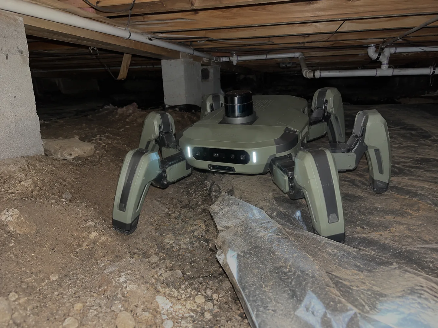A 20-centimeter legged robot inside a dark residential crawl space